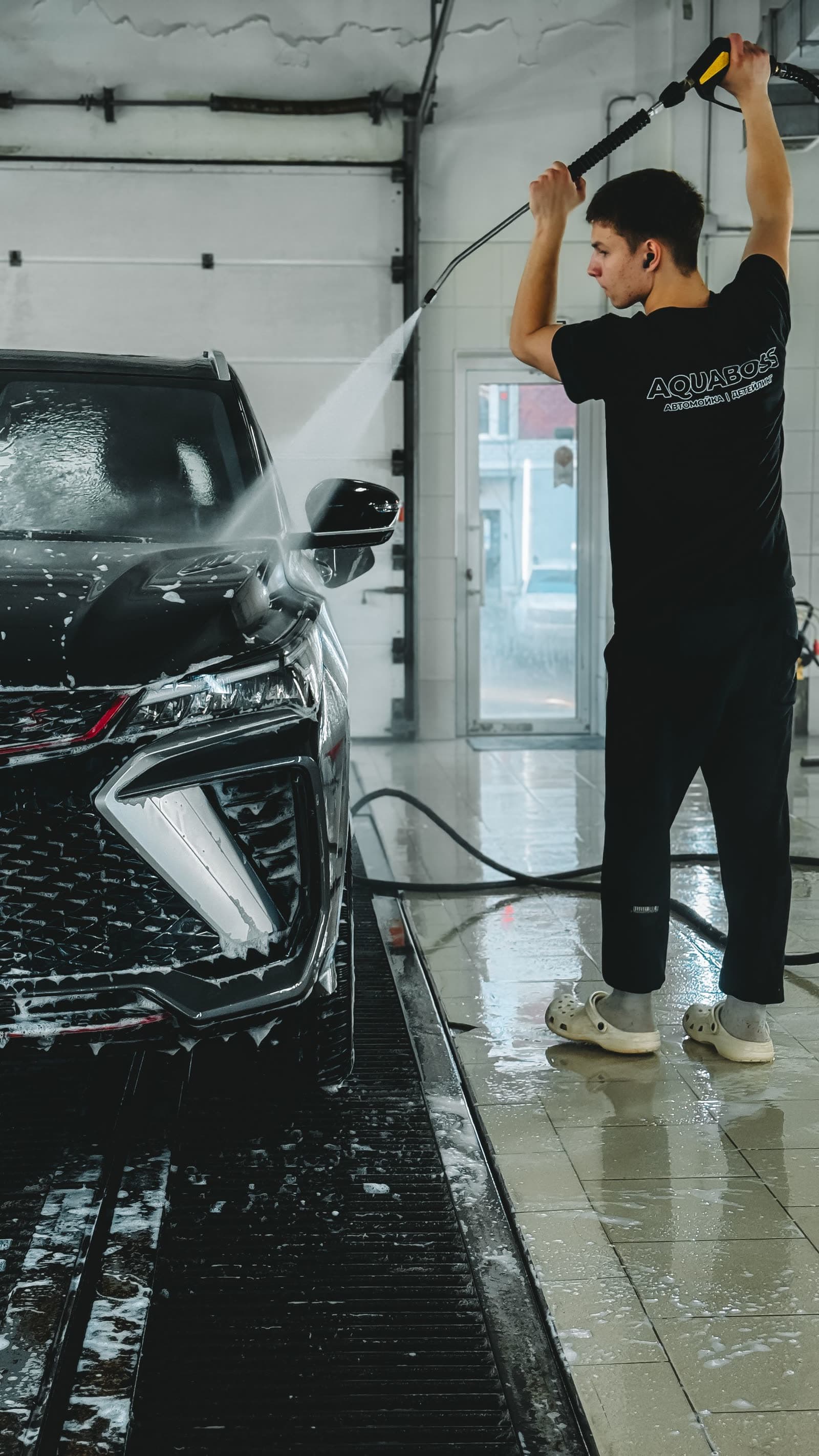 Detailer rinsing foam off a car in a wash bay